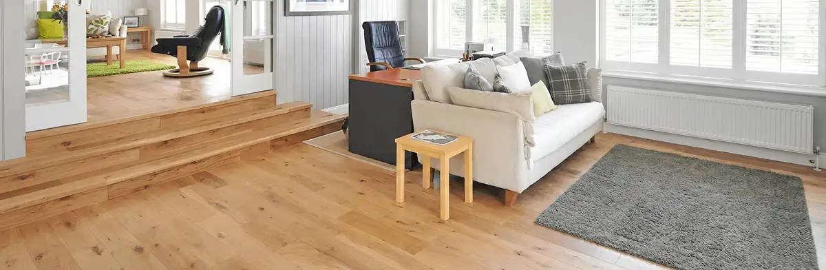 A modern living room with professionally installed laminate flooring, a beige sofa, a small side table, a gray rug, and large windows with white shutters in Providence, RI